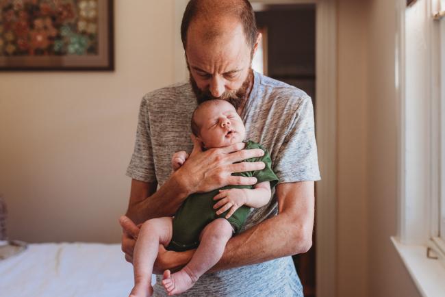 Father holding newborn baby and kissing his head during in-home Perth newborn lifestyle photography session