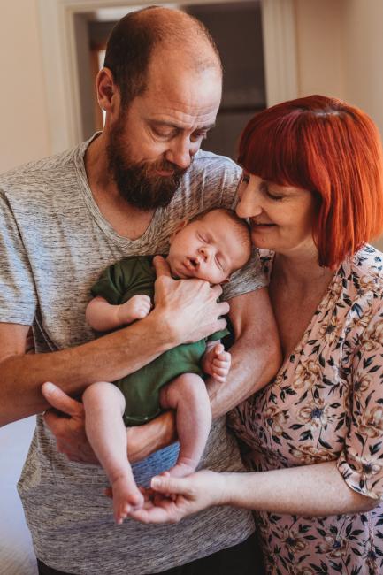 Father holding newborn baby as mother leans in to them during in-home Perth newborn lifestyle photography session
