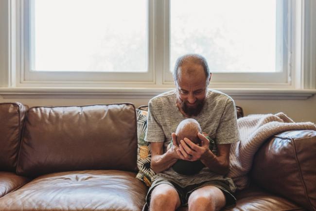 Father looking down at newborn baby on couch during newborn photography Perth session