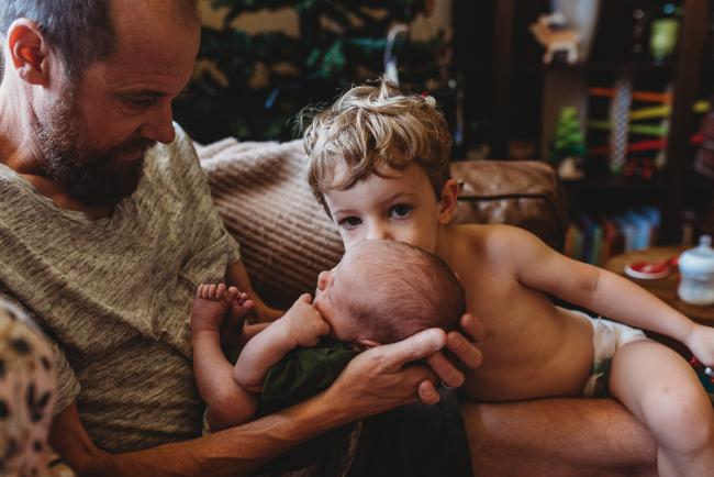 Little boy kissing newborn baby being held by father during in-home Perth newborn lifestyle photography session