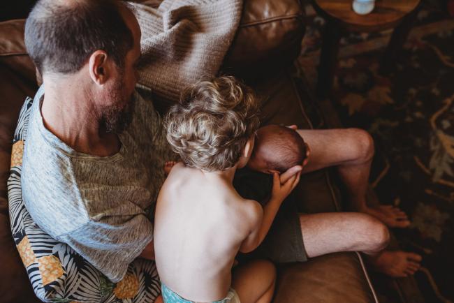 Little boy kissing newborn baby being held by father during in-home Perth newborn lifestyle photography session
