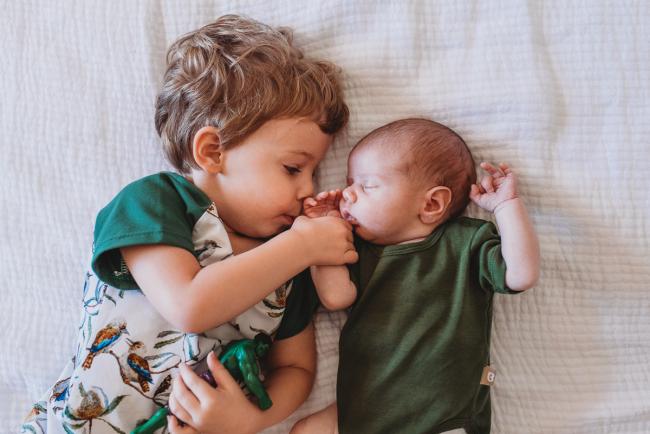 Brother holding newborn baby's hand during in-home Perth newborn lifestyle photography session