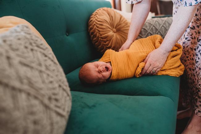 Baby in yellow wrap yawning during in-home Perth newborn lifestyle photography session