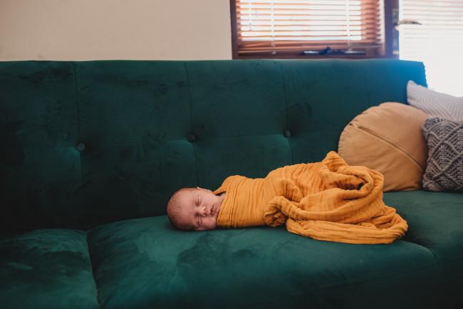 Baby in yellow wrap on couch during in-home Perth newborn lifestyle photography session
