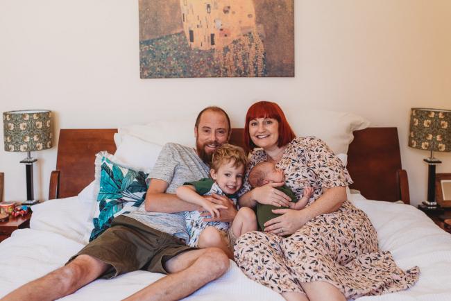 Parents on bed with newborn baby and toddler during in-home Perth newborn lifestyle photography session