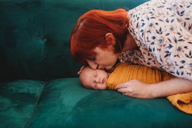 Mother leaning over to kiss newborn baby in wrap during in-home Perth newborn lifestyle photography session