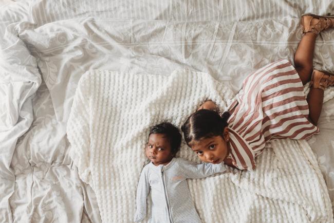 Top down image of toddler and baby on bed with in-home Perth lifestyle newborn photographer
