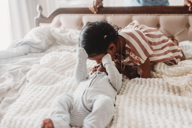 Little girl kissing newborn baby brother on the bed with in-home Perth lifestyle newborn photographer