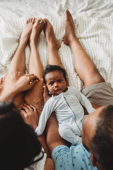 Newborn baby laying on parents laps with in-home Perth lifestyle newborn photographer
