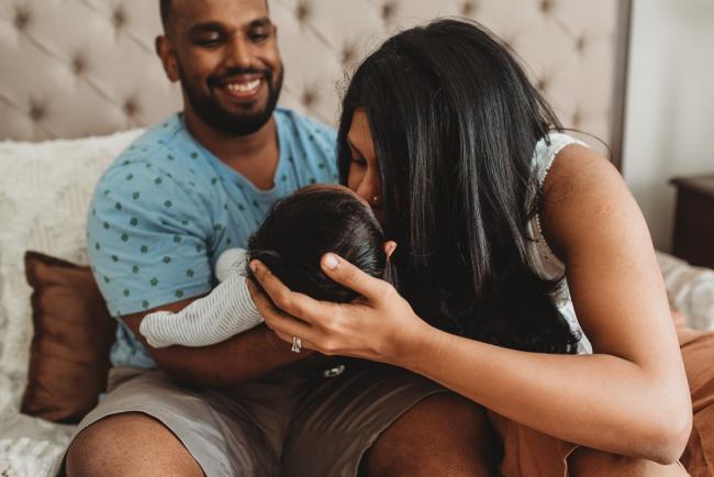 Mother kissing newborn baby being held by father with in-home Perth lifestyle newborn photographer
