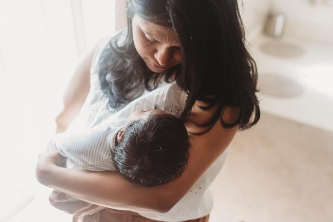 Mother holding newborn baby with in-home Perth lifestyle newborn photographer