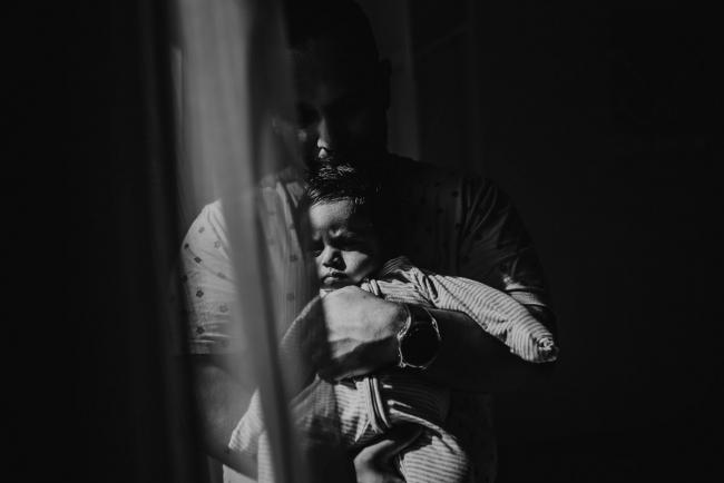 Black and white image of father holding newborn baby by window with in-home Perth lifestyle newborn photographer