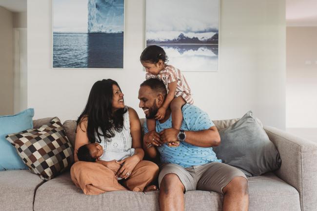 little girl on fathers shoulders with mother holding newborn baby on couch with Perth newborn photographer