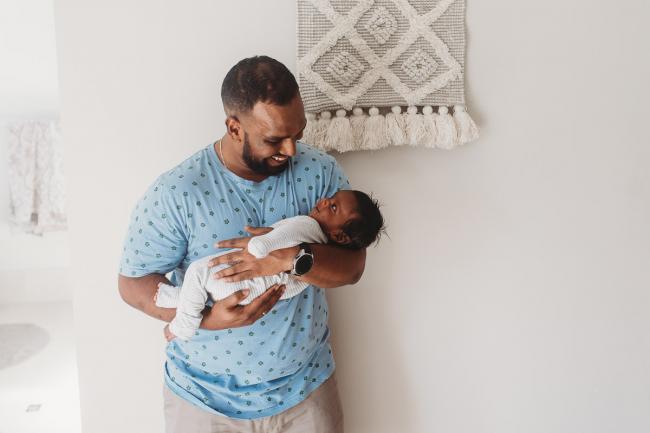 Father holding newborn baby who is looking up at him with in-home Perth lifestyle newborn photographer
