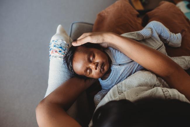 Top down image of newborn baby sleeping in mothers arms with in-home Perth lifestyle newborn photographer