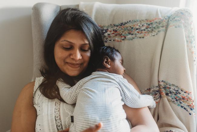 Mother smiling as newborn baby sleeps on her chest with in-home Perth lifestyle newborn photographer
