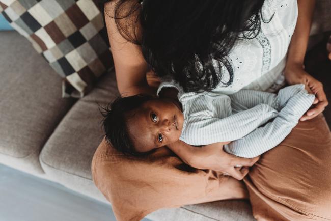 Newborn baby in mother's arms looking up at camera with in-home Perth lifestyle newborn photographer