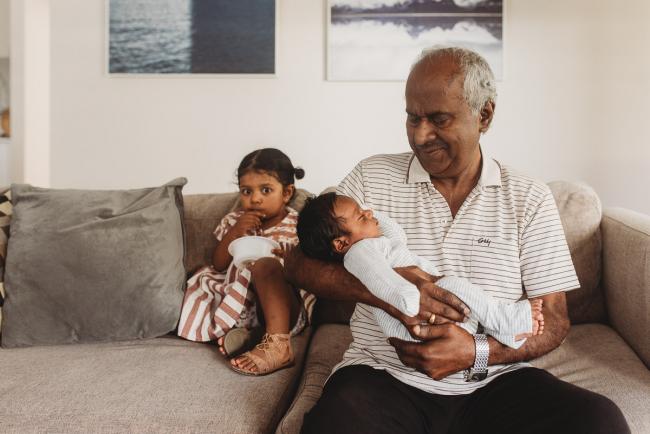 Grandfather holding newborn baby as granddaughter sits next to them with in-home Perth lifestyle newborn photographer