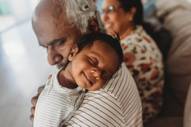 Newborn baby smiling in his sleep on grandfather's shoulder with in-home Perth lifestyle newborn photographer