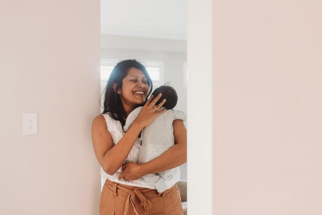 mother laughing and holding newborn baby in doorway with in-home Perth lifestyle newborn photographer