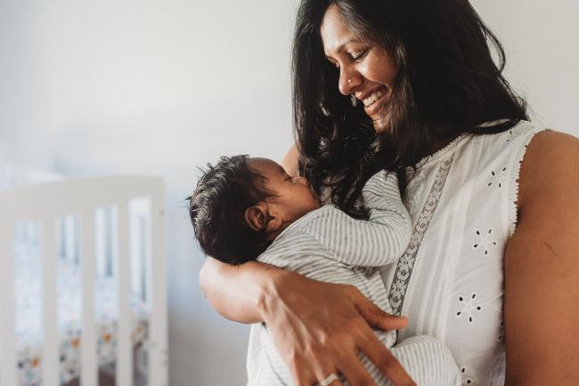 Mother smiling down at newborn baby with in-home Perth lifestyle newborn photographer