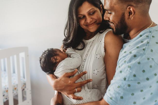 Parents smiling at each other as they hold newborn baby with in-home Perth lifestyle newborn photographer