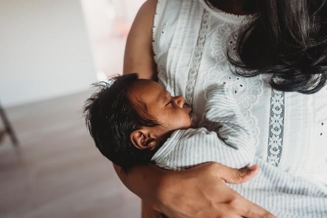 Newborn baby sleeping in mothers arms with in-home Perth lifestyle newborn photographer