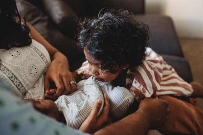Little girl leaning over to look at newborn baby with in-home Perth lifestyle newborn photographer