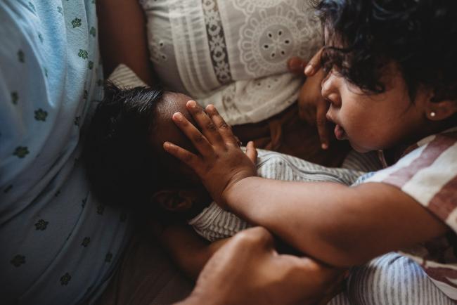 Little girl touching newborn baby's face with in-home Perth lifestyle newborn photographer