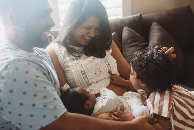 Parents on couch with newborn baby and daughter with in-home Perth lifestyle newborn photographer