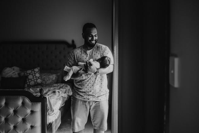 black and white image of father holding newborn baby with in-home Perth lifestyle newborn photographer