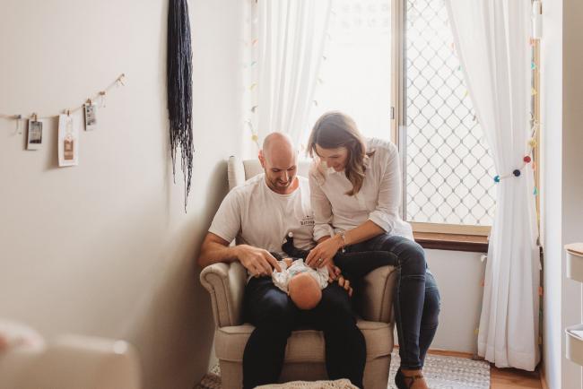 Parents on chair in nursery with baby with Perth newborn lifestyle photographer Alana Prosper Photography