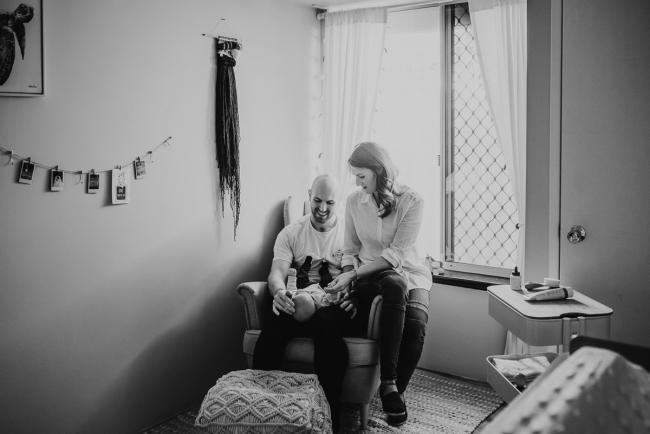 Black and white image of parents sitting on chair in nursery with Perth Newborn photographer Alana Prosper Photography