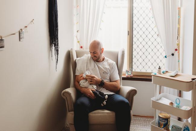 Father bottle feeding baby on chair in nursery with Perth Newborn photographer Alana Prosper Photography
