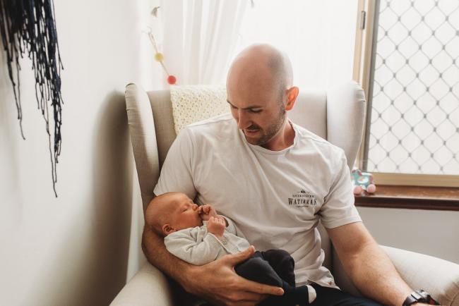 Father holding baby in chair in nursery with Perth Newborn photographer Alana Prosper Photography