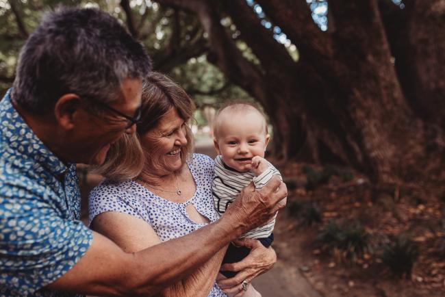 Baby smiling as being held by grandparents during extended family session at Hyde Park with Perth family photographer Alana Prosper Photography