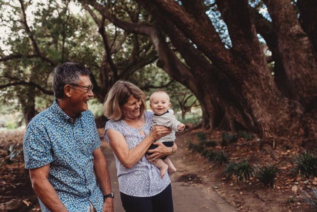 Baby smiling as being held by grandparents during extended family session at Hyde Park with Perth family photographer Alana Prosper Photography