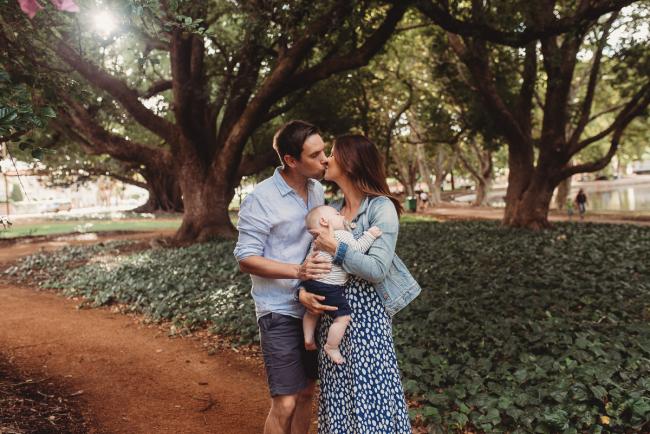 Parents kissing as they hold baby during extended family session at Hyde Park with Perth family photographer Alana Prosper Photography