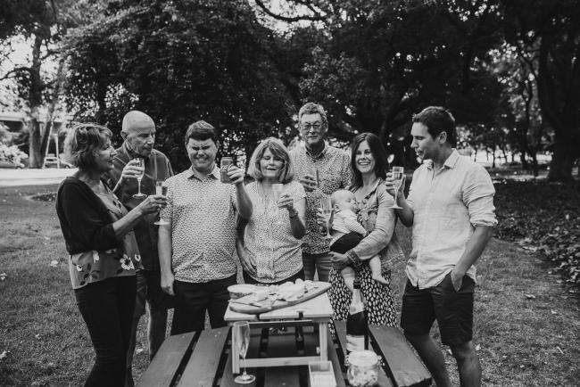 black and white image of extended family raising wine glasses during extended family session at Hyde Park with Perth family photographer Alana Prosper Photography