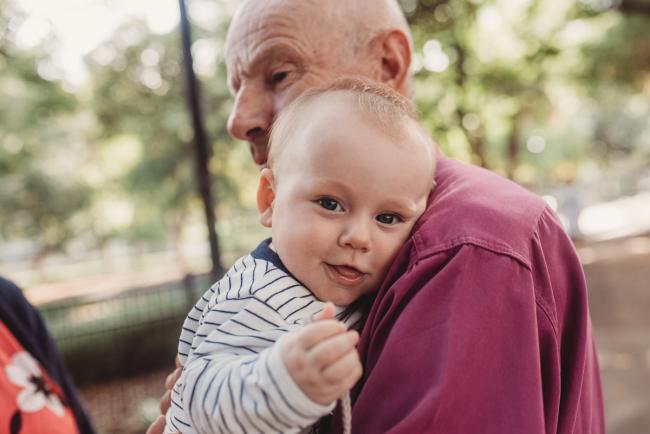 Baby smiling as being held by grandfather during extended family session at Hyde Park with Perth family photographer Alana Prosper Photography