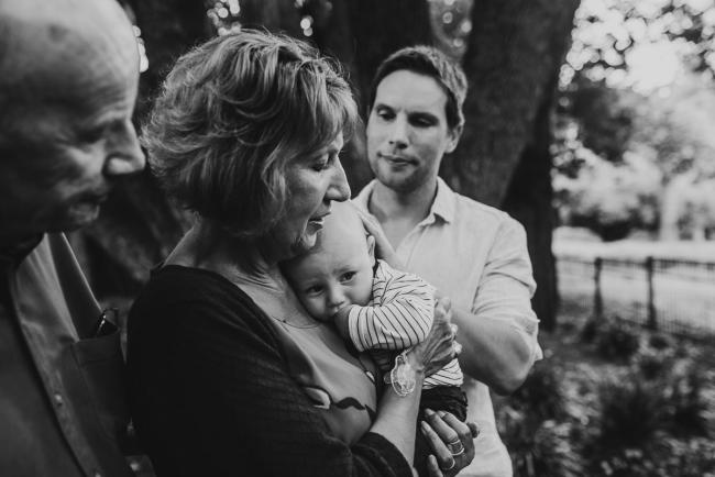 black and white image of baby resting on grandmother as grandfather and father lean in during extended family session at Hyde Park with Perth family photographer Alana Prosper Photography