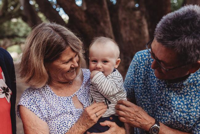 baby with hands in his mouth as being held by grandparents during extended family session at Hyde Park with Perth family photographer Alana Prosper Photography