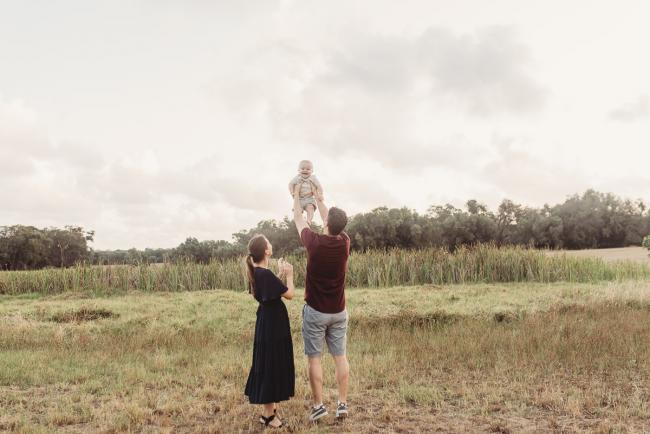 Father lifting baby in air with mother next to them with Perth Family Photographer Alana Prosper Photography at Perry's Paddock