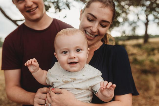 Baby smiling at the camera as being held by parents with Perth Family Photographer Alana Prosper Photography at Perry's Paddock