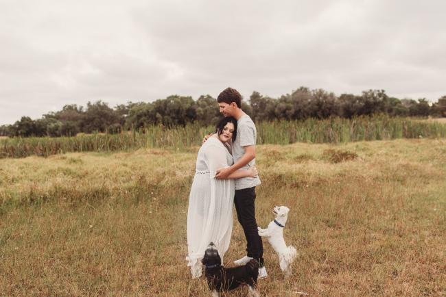 Pregnant couple hugging with dogs at their feet with Perth maternity photographer at Perry's Paddock