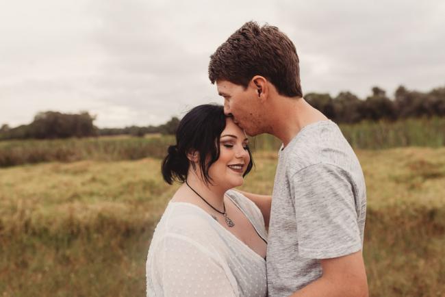 Man kissing pregnant partner's forehead with Perth maternity photographer at Perry's Paddock