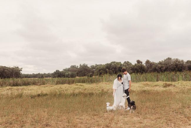 Pregnant couple in field with dogs at their feet with Perth maternity photographer at Perry's Paddock