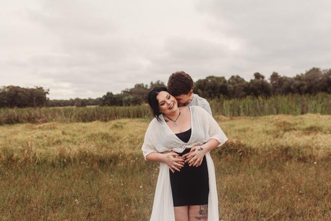 Man hugging pregnant partner from behind with Perth maternity photographer at Perry's Paddock