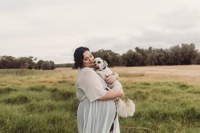 Pregnant woman holding white dog with Perth maternity photographer at Perry's Paddock