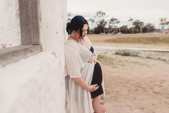 Pregnant woman leaning against white wall during Perth maternity photography session during golden hour at Perry's Paddock
